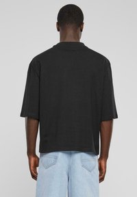 Black oversized t-shirt with short sleeves, featuring a crew neck and a smooth texture. Worn with light blue denim jeans.