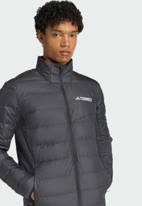 Grey insulated jacket with a high collar, zip closure, quilted texture, and a white "TERREX" logo on the left chest.