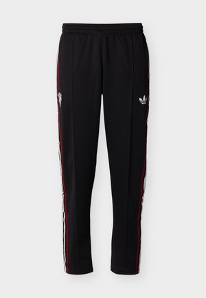 Juodos sportinės kelnės su elastine juosmens juosta, raudonomis ir baltomis šoninėmis juostomis bei „Adidas“ logotipu dešinėje šlaunyje.