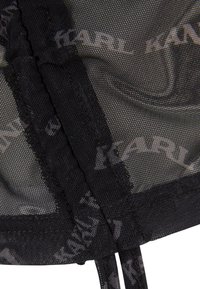 Svart mesh-stoff med "KARL" logo mønster. Har tynne sømmer og justerbare bånd for lukking. Teksturert overflate, semi-transparent utseende.