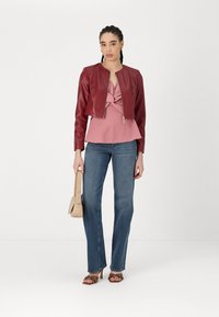 Giacca corta in pelle rossa, top annodato rosa, jeans a palazzo blu, sandali con tacco marroni, borsa beige. Stile minimalista e trame morbide.