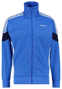Blå adidas träningsjacka med dragkedja fram, hög krage, tre vita ränder på axlarna och svarta detaljer på ärmarna. Mjuk, sportig tyg.
