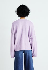 Maglione viola a maglia con spalle scese, orlo a coste e texture morbida, abbinato a jeans larghi blu. Solo vista posteriore.