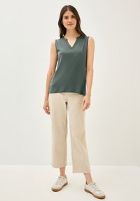 Top sin mangas de color verde oscuro con un diseño de escote en V, combinado con pantalones de pierna ancha en un tono beige claro y zapatillas de color claro. Conjunto sencillo y casual.