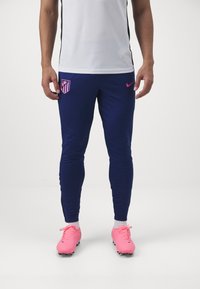 Tengeri kék sportnadrág rózsaszín Nike logóval és Atlético Madrid címerrel, szűkített fazon, elasztikus anyag, világos rózsaszín focicipővel párosítva.