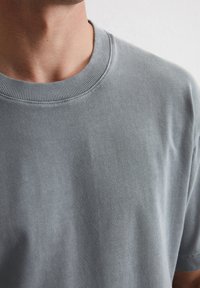 T-shirt en coton bleu clair avec un col ras de cou côtelé. Le tissu a une texture lisse et une coupe décontractée, montrant des détails de coutures subtils.