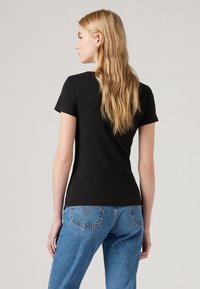 Black short-sleeve t-shirt with a fitted design, made of soft material. Paired with high-waisted light blue denim jeans.