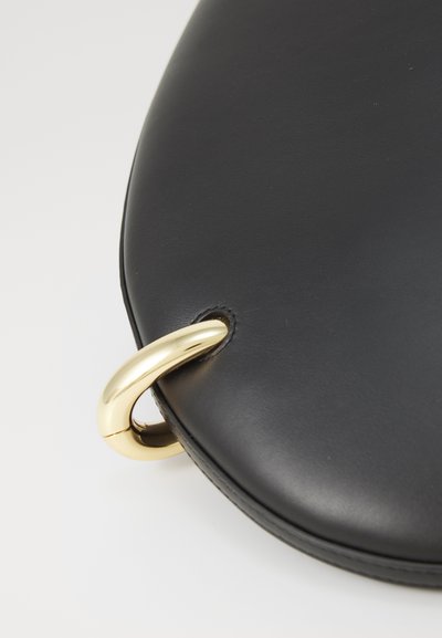 Fekete bőrtáska sima textúrával, kerek formával és arany fémgyűrű díszítéssel az élein.