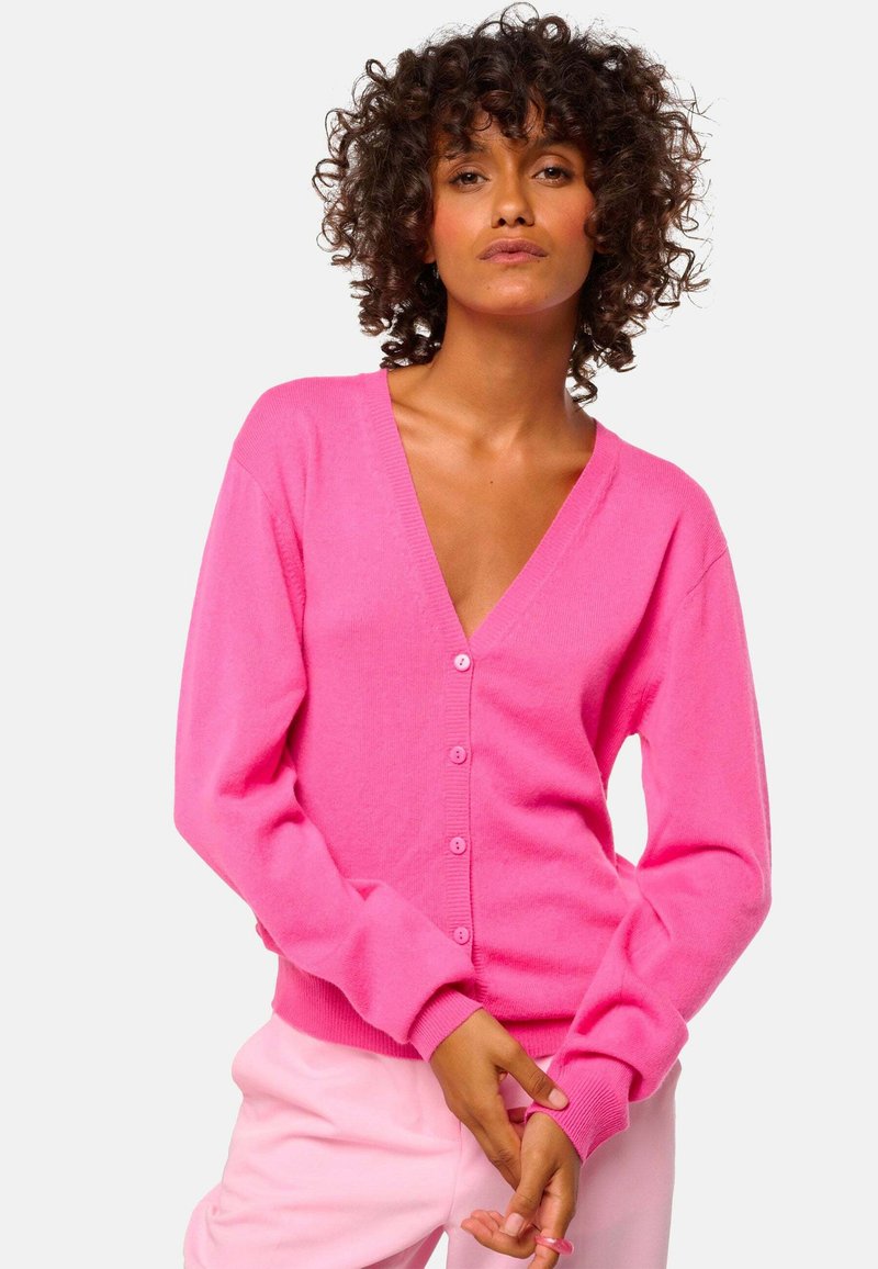 Cardigan fuchsia en matériau doux, avec un décolleté en V profond, des manches longues et six boutons sur le devant. Poignets et ourlet côtelés.