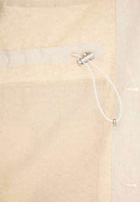 Tessuto beige con un cordino elastico bianco fissato da una chiusura a scatto argentata inserita in un anello di tessuto.