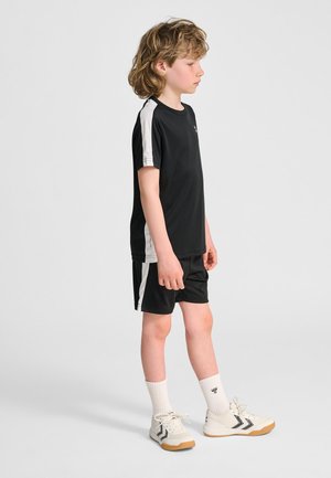 Svart sportset med kortärmad tröja med vita detaljer och matchande shorts. Bärs med ljusa sneakers och vita strumpor.