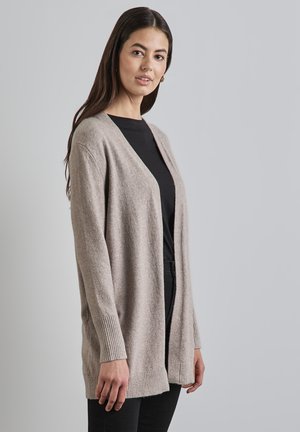Cardigan ouvert beige clair en mélange de laine douce, présentant une coupe décontractée, des poignets côtelés et une texture lisse. Porté sur un haut noir.