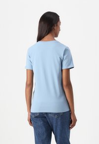 Tricou din bumbac de culoare albastră deschisă, cu mâneci scurte și guler rotund. Materialul are o textură moale. Design simplu, fără modele sau accente vizibile.