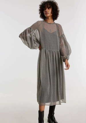 Zwart-wit geruite midi-jurk met pofmouwen, transparant materiaal en een geplooide taille. Draagt met zwarte enkellaarsjes.