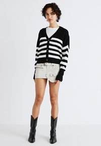 Black and white striped, knitted cardigan with a v-neck, five buttons, and oversized sleeves, paired with beige shorts and black boots.