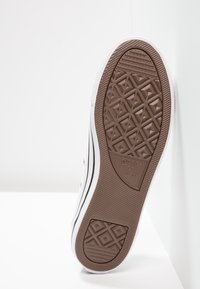 Brown rubber outsole of a sneaker with a diamond pattern, white sidewalls, and black stripe accents. Brand logo visible on the sole.