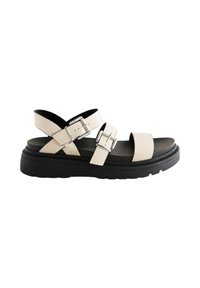 Beige sandalen met bandjes en twee verstelbare gespen, een dikke zwarte zool en een gladde textuur. X-vormige bandjes bieden steun.