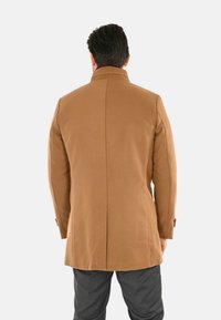 Cappotto in misto lana marrone con vestibilità su misura, colletto alzato e spacco singolo sul retro, dotato di polsini con bottone e una superficie liscia.