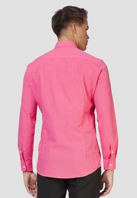 Camicia a maniche lunghe in tessuto rosa brillante, con colletto a bottoni e polsini abbottonati, caratterizzata da una texture morbida e un orlo leggermente curvo.