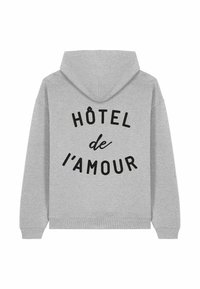 Felpa grigia con tasca a marsupio, con testo nero che dice "HÔTEL de l'AMOUR" disposto in modo curvo sulla parte posteriore.