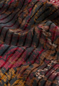 Textile with a textured surface featuring dark colors, stripes, and a blurred pattern of red, brown, and yellow hues in a wavy arrangement.