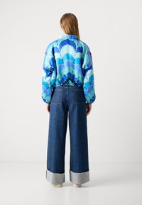 Giubbotto imbottito blu con motivo a scaglie; abbinato a pantaloni in denim a gamba larga con orlo in denim chiaro. Tessuti testurizzati ovunque.