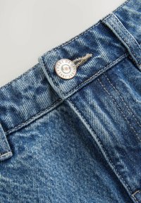 Hele denim teksased, mis on kerge sinise värvusega koos pleekinud aladega, messingist nööbiga kinnitamine ja kontrastne õmblus vöökohal.