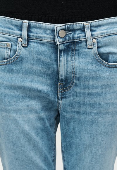 Μπροστινή όψη ανοιχτό μπλε τζιν τζιν παντελονιού που δείχνει κουμπί, φερμουάρ, θηλιές για ζώνη και μπροστινές τσέπες πάνω σε μαύρο φόντο.