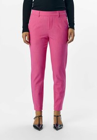 Pantalons roses ajustés avec plis à l'avant et poches latérales, fabriqués en tissu texturé. Associés à des escarpins noirs à bout pointu.