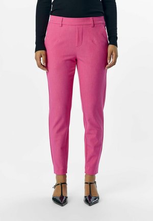 Pantaloni rosa aderenti con pence frontali e tasche laterali, realizzati in tessuto testurizzato. Abbinati a décolleté nere a punta.