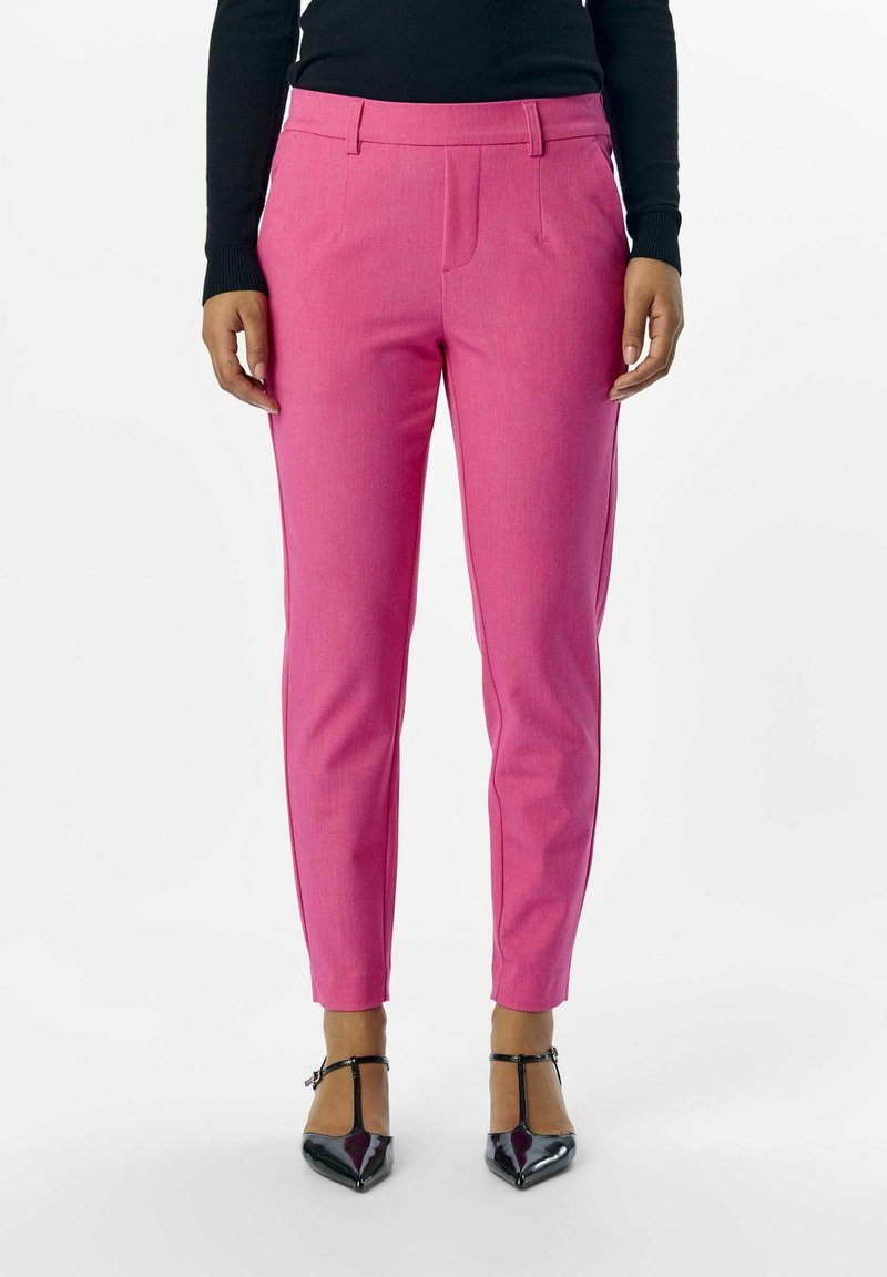 Pantalons roses ajustés avec plis à l'avant et poches latérales, fabriqués en tissu texturé. Associés à des escarpins noirs à bout pointu.