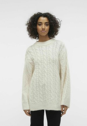 Sweter w sploty w kolorze off-white, z wysokim dekoltem i szerokimi rękawami, o miękkim, teksturowanym wyglądzie i luźnym kroju.