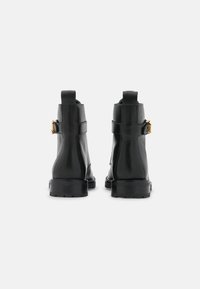 Botas de tobillo de cuero negro con un acabado suave, con detalle de hebilla lateral, suela resistente y una asa en la parte trasera.