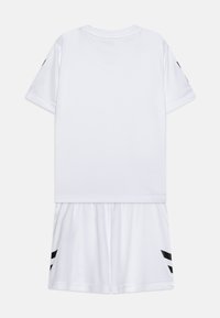 Tenue de sport blanche comprenant un T-shirt à manches courtes et un short à taille élastique. Rayures noires sur les manches et le short. Texture lisse.