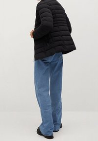 Zwarte pufferjack met horizontaal gestikt patroon, gecombineerd met lichtblauwe jeans en zwarte schoenen, gezien van achteren.