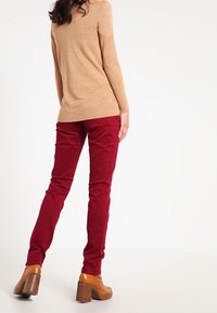 Suéter color tostado, con silueta ajustada, combinado con pantalones burdeos de cintura alta y botas marrones de tacón. Enfasis en texturas suaves y colores cálidos.