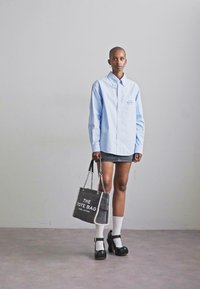 Chemise rayée bleu clair avec fermeture à boutons ; mini jupe grise ; chaussures à talons noirs ; chaussettes blanches ; sac fourre-tout gris avec texte blanc.