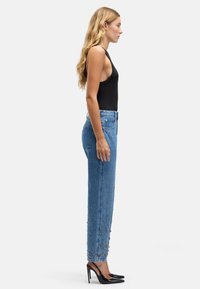 Niebieskie dżinsy z wysokim stanem o prostej nogawce, zdobione srebrnymi ćwiekami na dole. Połączone z dopasowanym czarnym tank topem i czarnymi szpilkami.