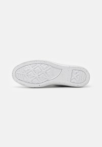 Biała gumowa podeszwa sportowego buta z geometrycznym wzorem bieżnika, lekko poszarpaną teksturą oraz logo Converse All Star w pobliżu łuku stopy.