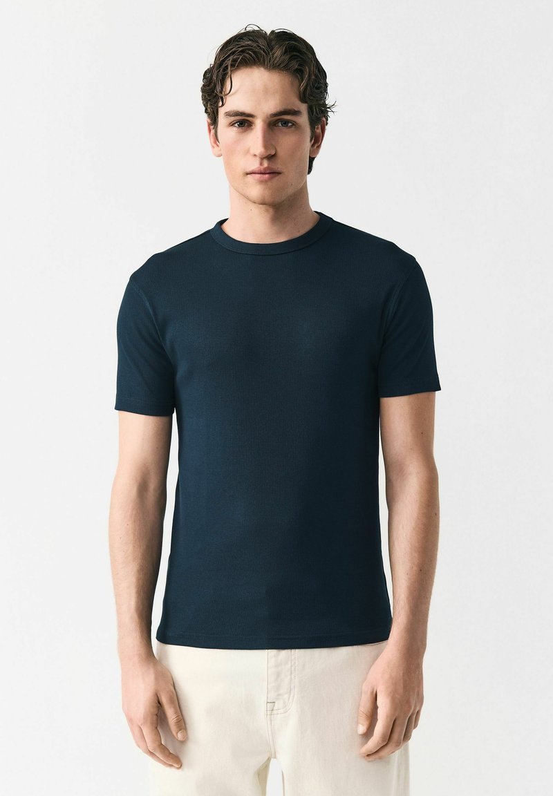 Marineblauw geribd T-shirt met korte mouwen en een ronde halslijn, met een aansluitend ontwerp en een zachte textuur, gedragen met lichtgekleurde broeken.