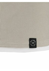 Grijze textuurstof met een ribbelpatroon, voorzien van een witte zoom en een zwart etiket met de tekst "Key Largo sinds 1994."
