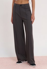 High-waisted, wide-leg trousers in dark gray fabric with a smooth texture, featuring a front button closure and pleats.