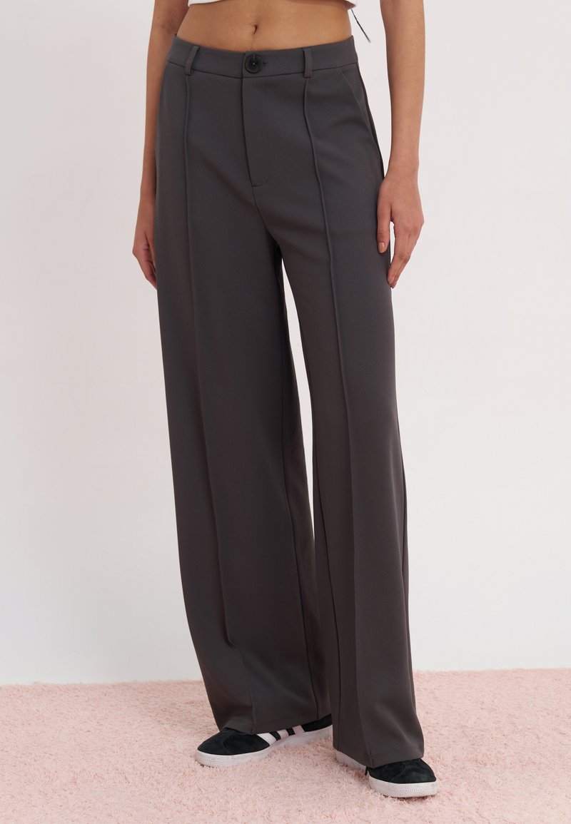 High-waisted, wide-leg trousers in dark gray fabric with a smooth texture, featuring a front button closure and pleats.