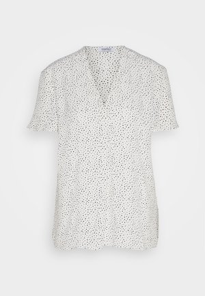 Blouse blanche à manches courtes avec un décolleté en V, ornée d'un motif de petits points noirs éparpillés. Fabriquée en tissu léger, elle possède une coupe décontractée et des fentes sur les côtés.