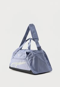 Αθλητική τσάντα duffel σε ανοιχτό μοβ με μαύρη βάση, διπλές λαβές, ρυθμιζόμενο λουρί ώμου, πλαϊνή τσέπη με φερμουάρ και λογότυπο Puma με κίτρινες ρίγες.