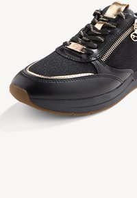Sneaker nera con tomaia in mesh, cerniera con accenti dorati e dettagli in pelle texturizzata. Presenta lacci e una suola in gomma color beige.