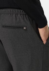 Pilkos sportinės kelnės su minkšta tekstūra, elastinga juosta juosmens srityje, šoninėmis kišenėmis ir mažu metaliniu logotipo akcentu.