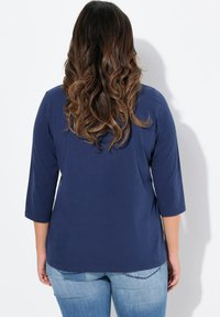 Mörkblå, topp med medellång ärm och avslappnad passform. Mjuk, slät textur. Kombineras med ljusblå jeans, fokus på minimala designelement.