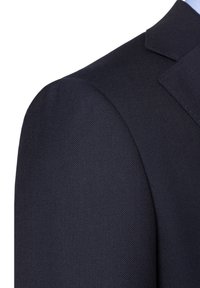 Faktura ciemnoniebieskiego materiału garniturowego z widocznym splotem. Zbliżenie na obszar ramienia z dopasowanym krojem i wyraźnymi detalami klap.