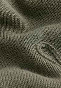 Țesătură tricotată verde cu un model texturat, având o buclă proeminentă. Material moale, asemănător lânii, care evidențiază o culoare subtilă și estompată.